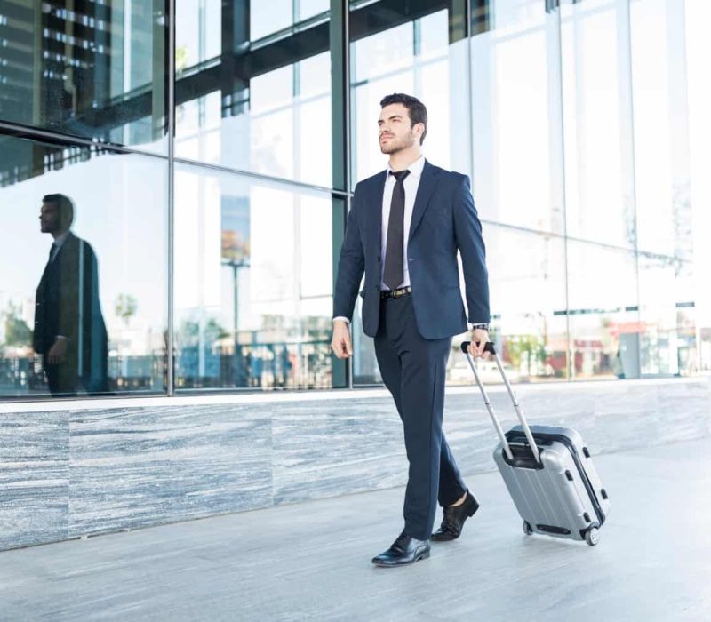 full-length-handsome-young-man-suit-walking-with-luggage-outside-office-building